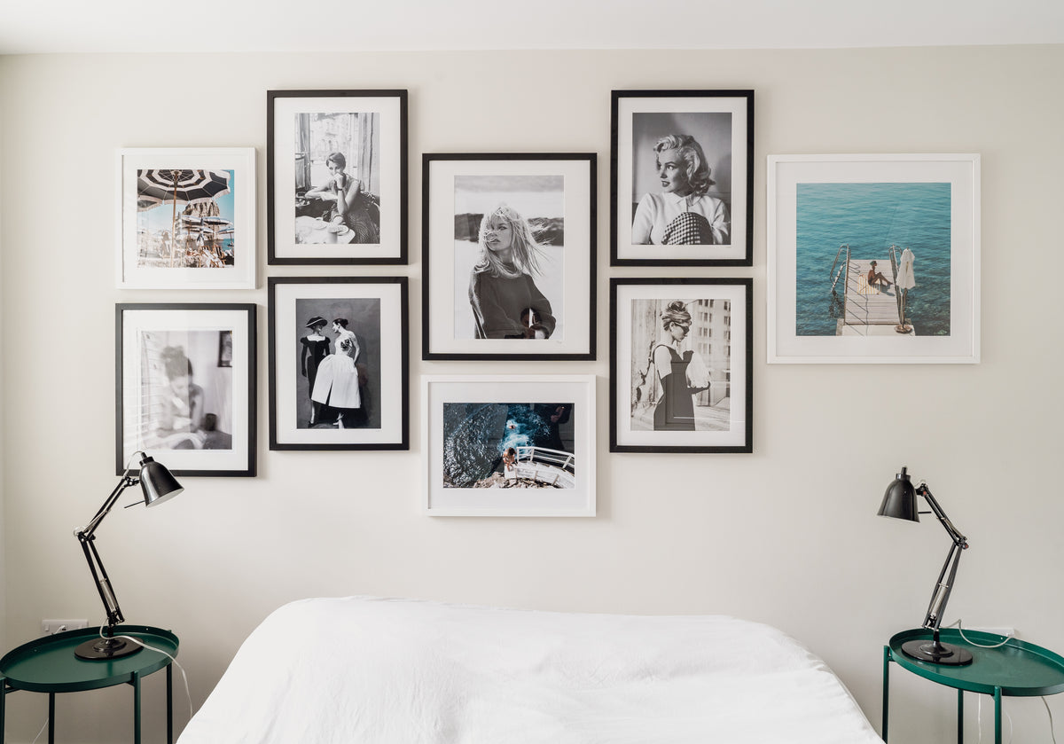 Gallery wall of black and white framed Sonic Editions photographs above a bed with two green side tables