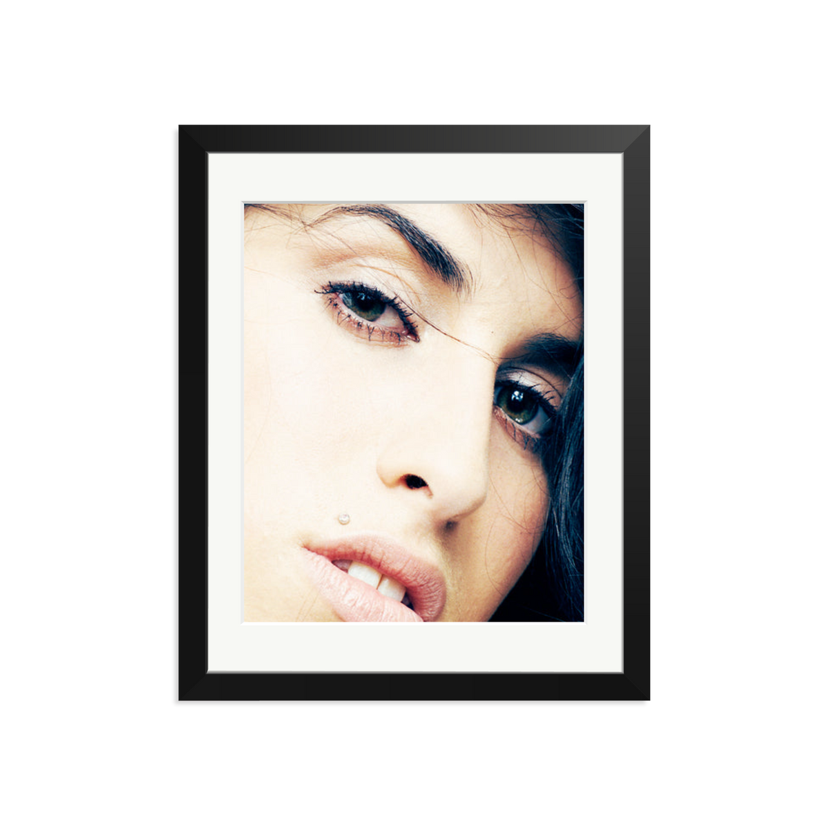 A close-up portrait photograph of a woman's face in a black frame with white mat, shot with warm, soft lighting that emphasizes skin texture and eye detail.